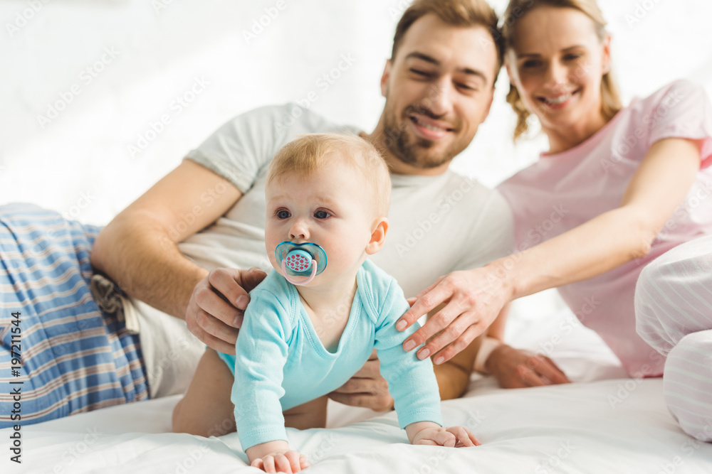 Smiling parents touching infant daughter with baby dummy