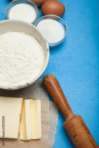 Sweet baking - the ingredients of the dough recipe (eggs, flour, milk, butter, sugar) on a blue table. Background layout.