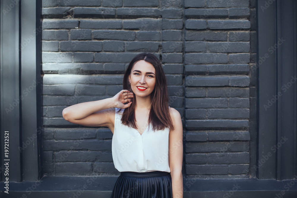 Young brunette woman with red lips wearing black skirt and white blouse smiling wide. Girl, black brick wall background, copy space, closeup Young brunette woman with red lips wearing black skirt and white blouse smiling wide. Girl, black brick wall background, copy space, closeup