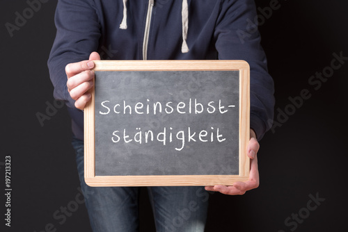 Arbeiter hält eine Tafel hoch auf der Scheinselbständigkeit steht