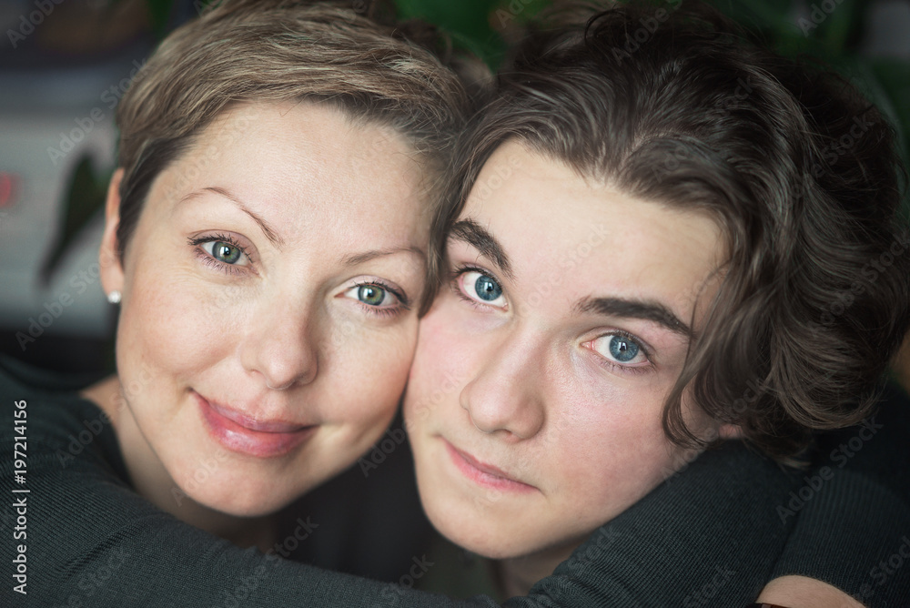 Happy young mom with short hair hugs her teenage son and smiles. A boy looks sad eyes. Happy young mom with short hair hugs her teenage son and smiles. A boy looks sad eyes.