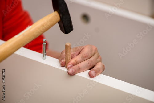 Close up on hands hammering a wooden peg in furniture.