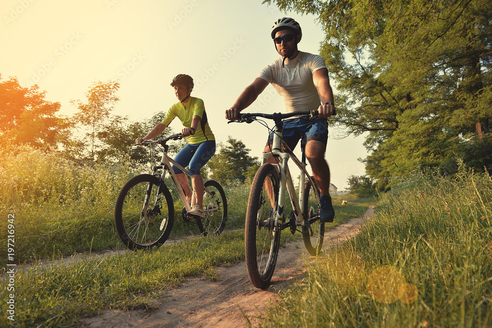 a woman and a man cycling in summer in the park on bicycles