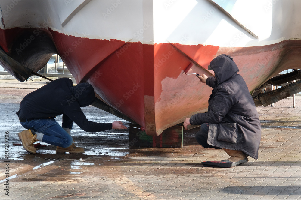 Men painting hull of a fishing boat out of the water. Stock Photo