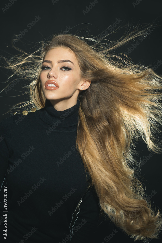 Fashion woman hair style. Haircare and health concept. Stylish blonde woman  waving hair on wind, wearing in black sweater. Beautiful girl face makeup.  Luxury look. Sensual model on black background. Stock Photo |