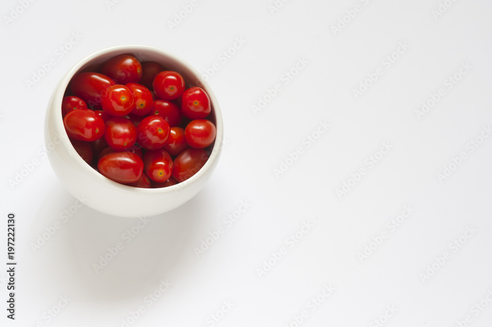 Some red plum tomatoes in a round white bowl on a white background Some red plum tomatoes in a round white bowl on a white background