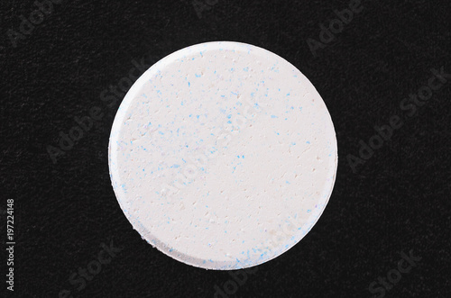 White rounded chlorine tablet isolated on a dark textured background. photo
