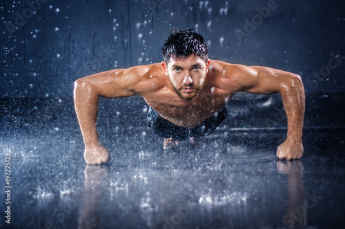 Handsome half-naked young sexy fit muscular athlete performing push-ups under the rain