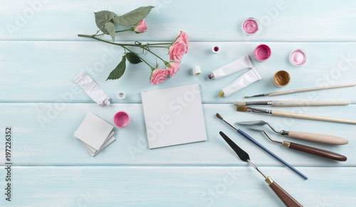 Workplace with canvas, paintbrushes, roses and paints on wooden boards