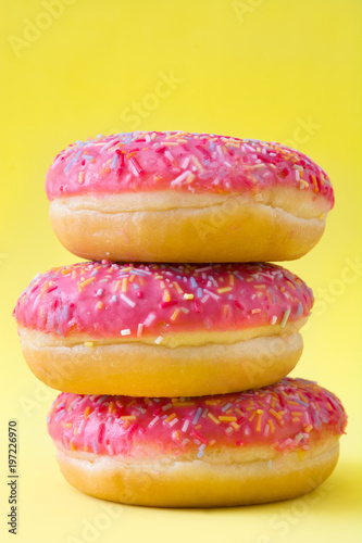Pink frosted donut with colorful sprinkles on yellow background.