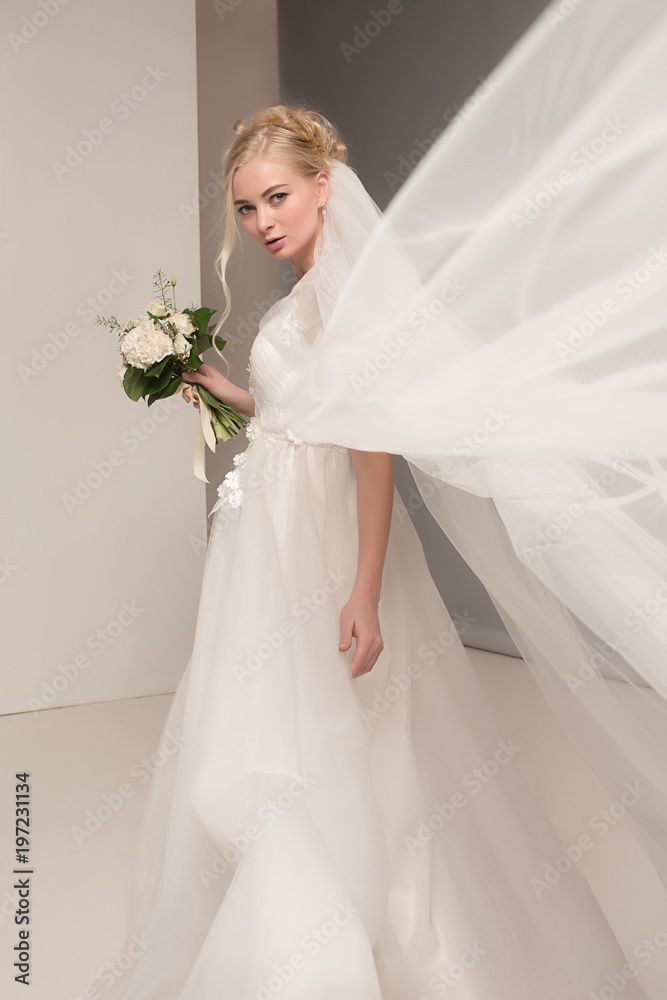 Bride in beautiful dress standing indoors in white studio interior like at home. Trendy wedding style shot. Young attractive caucasian model like a bride tender looking. Bride in beautiful dress standing indoors in white studio interior like at home. Trendy wedding style shot. Young attractive caucasian model like a bride tender looking.