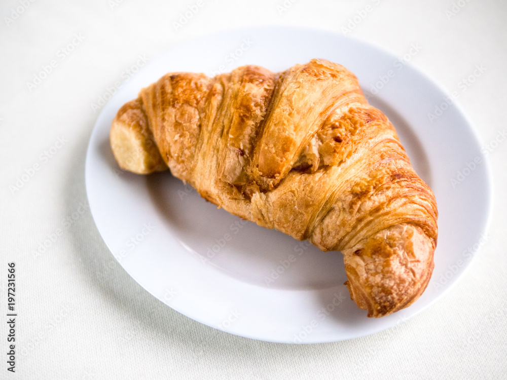 Single croissant on a white plate and background Single croissant on a white plate and background