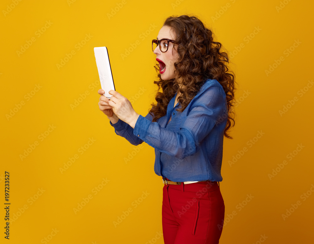 modern shocked woman isolated on yellow using tablet PC modern shocked woman isolated on yellow using tablet PC