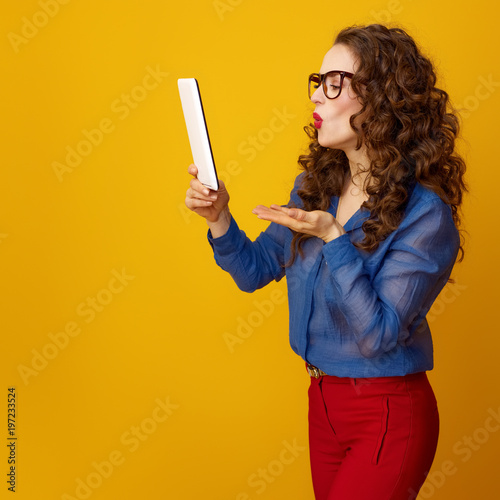 woman against yellow background with tablet PC blowing air kiss