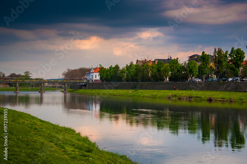 River Uzh in Ukraine, Uzhgorod. Trees, city, bridge and cloudy sky reflected in water