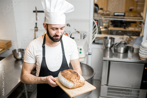 Portrait of a handsome baker in uniform standing with fresh bread in the small bakery manufacturing