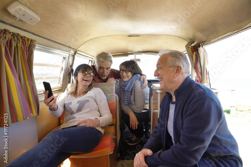 Group of senior friends in camper van using smartphone