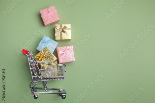 Colorful gifts box, supermarket shopping cart on green background