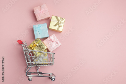 Colorful gifts box, supermarket shopping cart on pink background