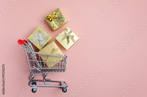 Colorful gifts box, supermarket shopping cart on pink background