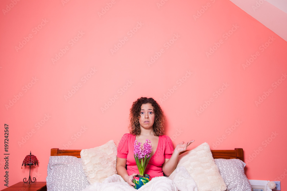 Surprised woman holding flowers in the bed on pink background