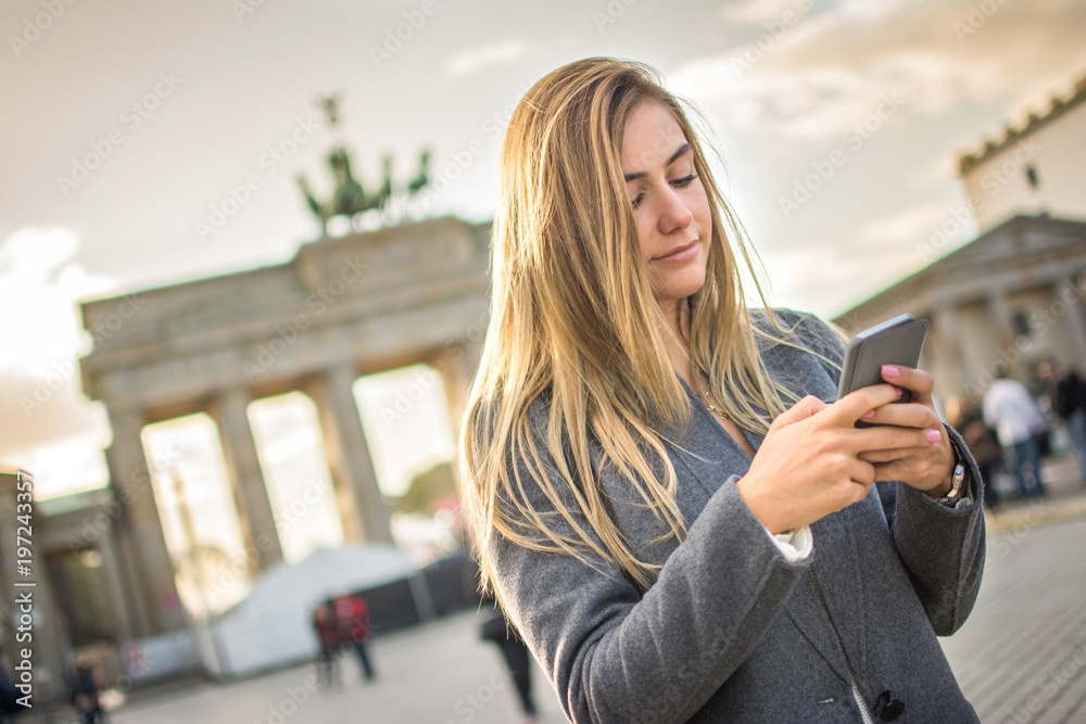 Beautiful blonde hair girl using phone in front of Brandenburg Gate in Berlin, Germany,