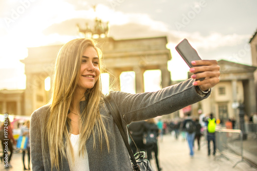 Beautiful blond girl taking selfie in front of Brandenburg Gate in the city of Berlin, Germany.