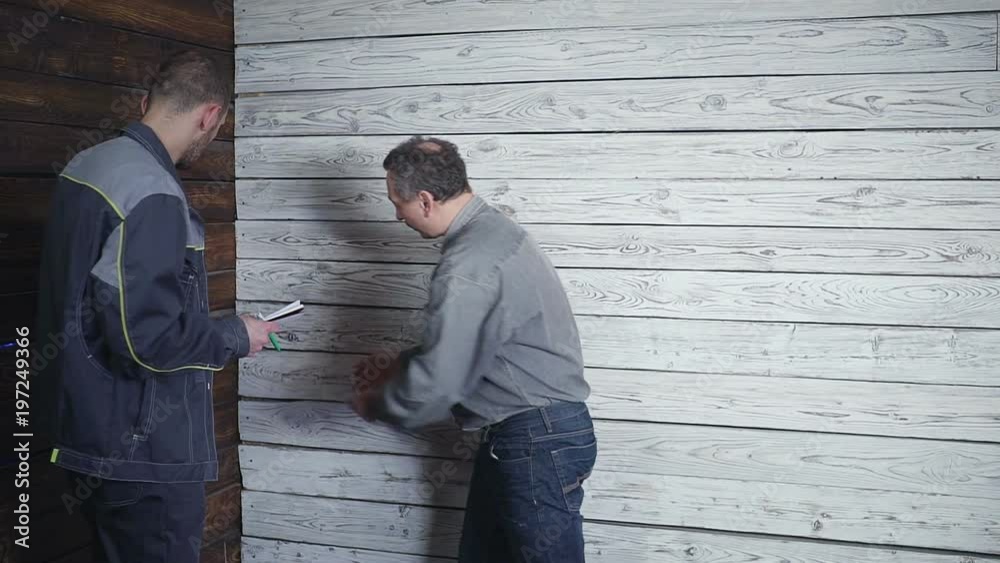 worker and the demanding customer to discuss and swear on the background of a wooden wall. Problem in construction.