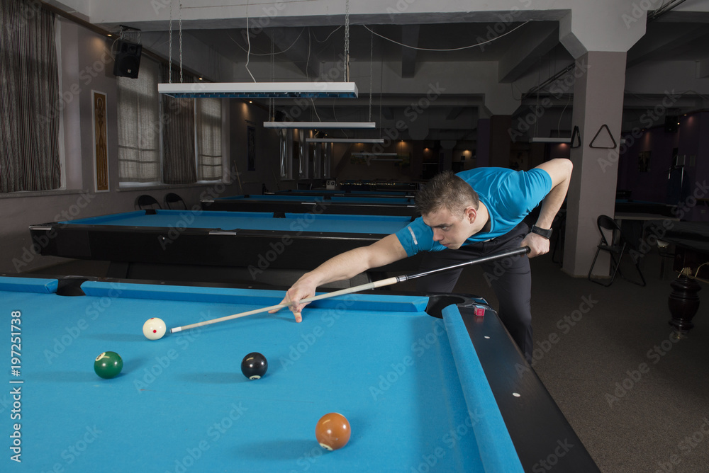 Fototapeta premium Side view of a pool player performing a shot on a ball with chalk on the side of the table.