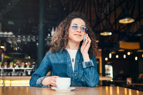 Woman with curly hair sitting near window with mobile phone and comunicate.