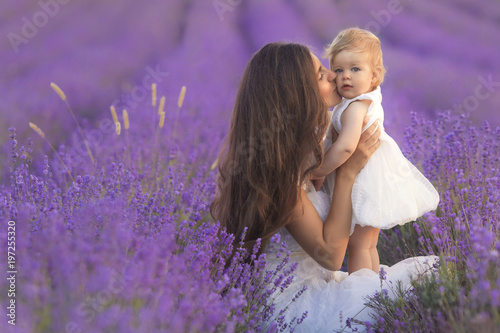 Happy beautiful mother and cute little daughter have fun in aroma lavender fields. Family holiday in summer day.