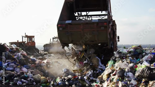 Garbage truck unloads garbage to the dump.Bulldozers work in the background photo