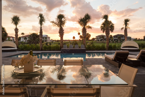 Outdoor dining area overlooking pool and palm trees at sunset
