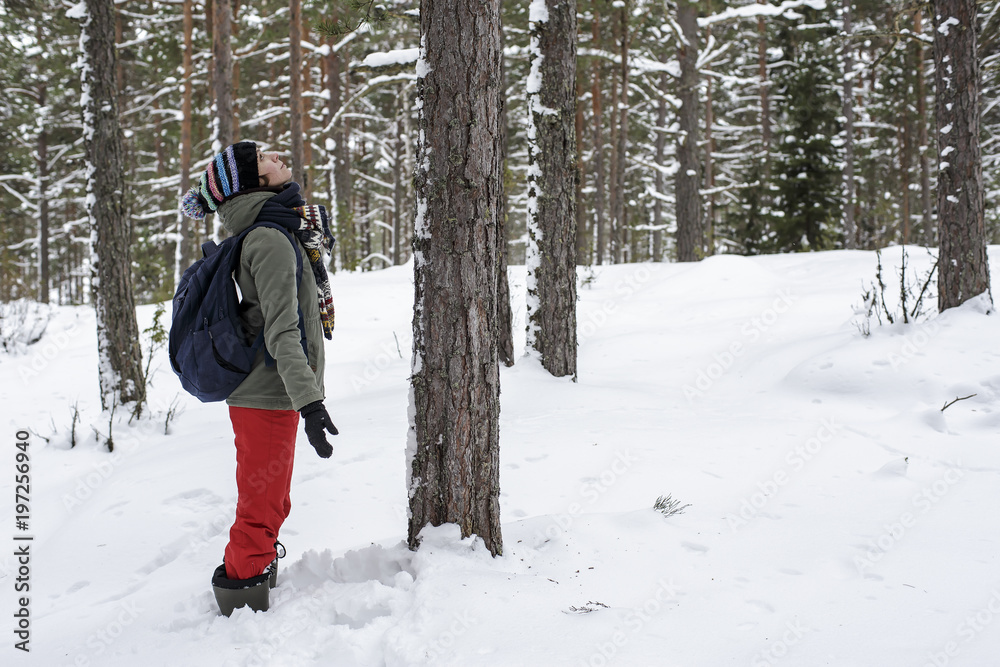 A nice smiling woman is standing, holding out her hands to the sides and admiring the winter, snow-covered forest. The concept of conservation of nature.