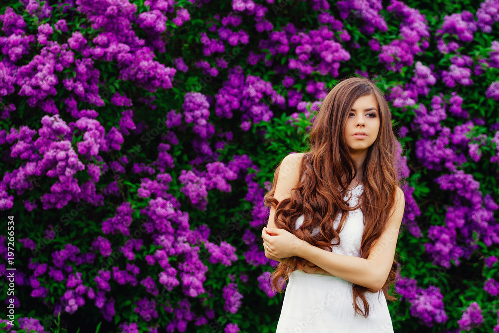 Happy beautiful young woman with long hair in a blooming spring Park, the charming girl in a white dress with bright flowering trees, the girl on the background of flowering gardens
