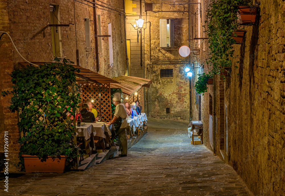 Medieval narrow cozy street with tables of restaurant in Siena, Tuscany, Italy