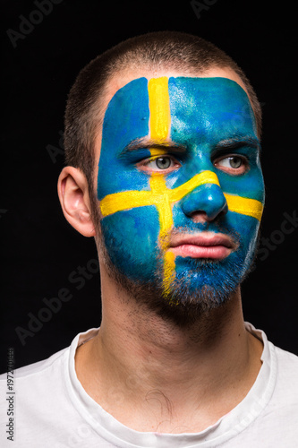 Portrait of handsome man face supporter fan of Sweden national team with painted flag face isolated on black background. Fans emotions.