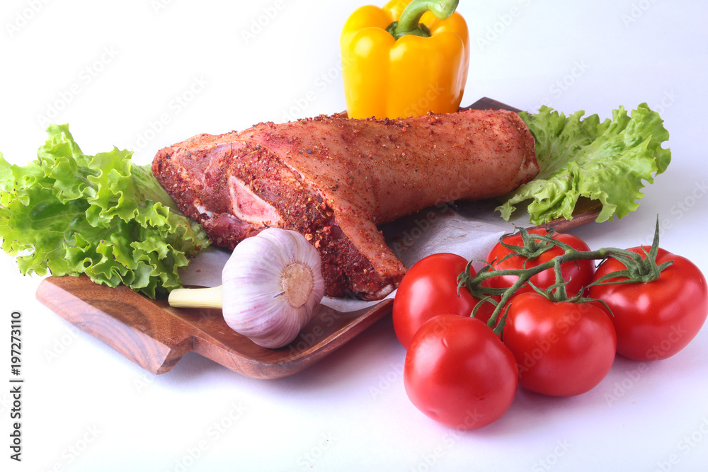 Raw pork knuckle and vegetables, garlic, tomatoes, bell pepper. spices and lettuce leaves on a cutting board. Selective focus. Ready for cooking. Raw pork knuckle and vegetables, garlic, tomatoes, bell pepper. spices and lettuce leaves on a cutting board. Selective focus. Ready for cooking.