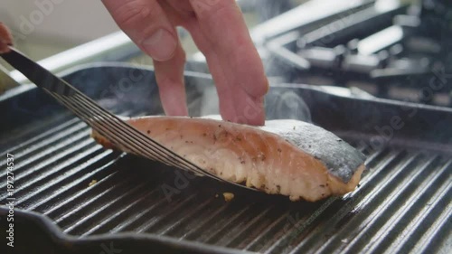 Man Roasting Fish With Spatula On Grill Pan In Kitchen