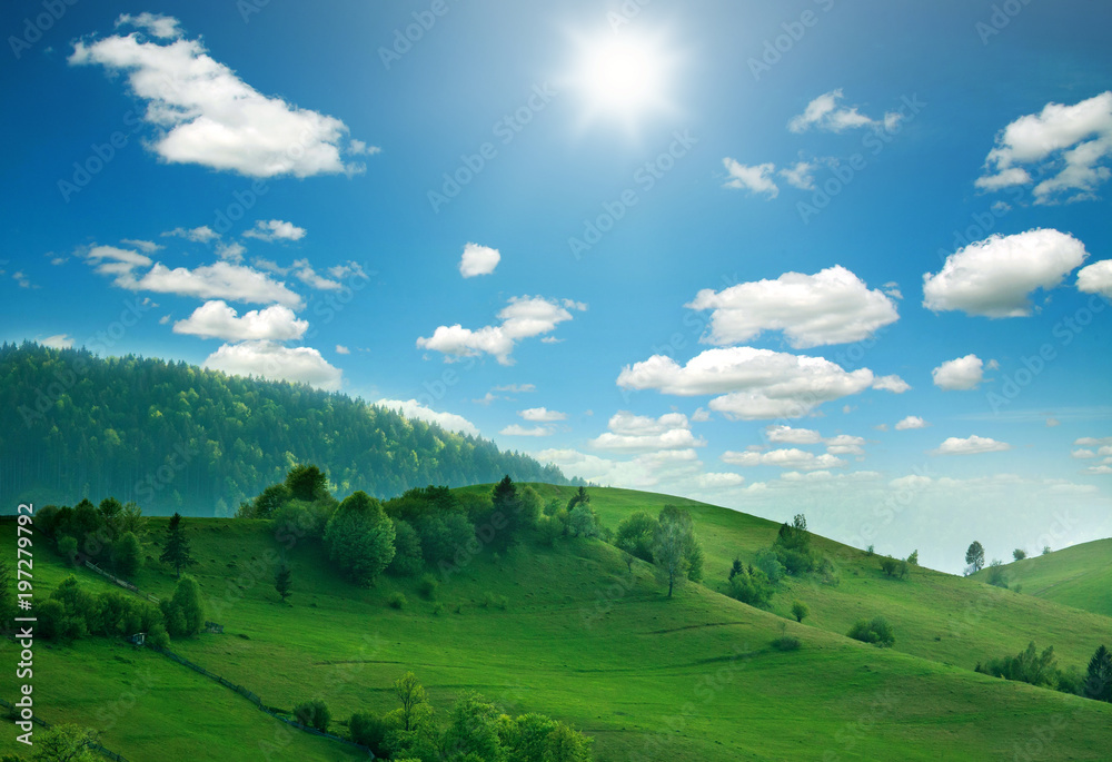 Mountain hills and green fields in sunlight on sky clouds