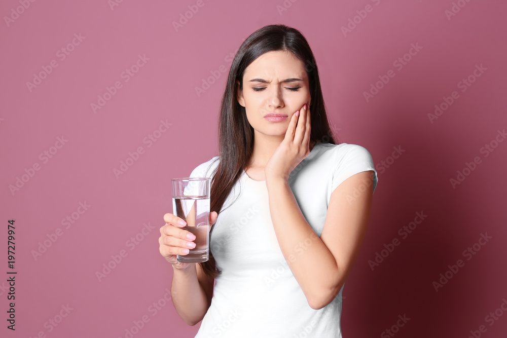 Young woman with sensitive teeth and glass of cold water on color background Young woman with sensitive teeth and glass of cold water on color background
