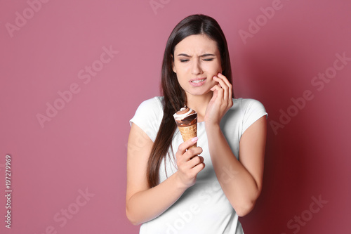 Young woman with sensitive teeth and cold ice cream on color background photo