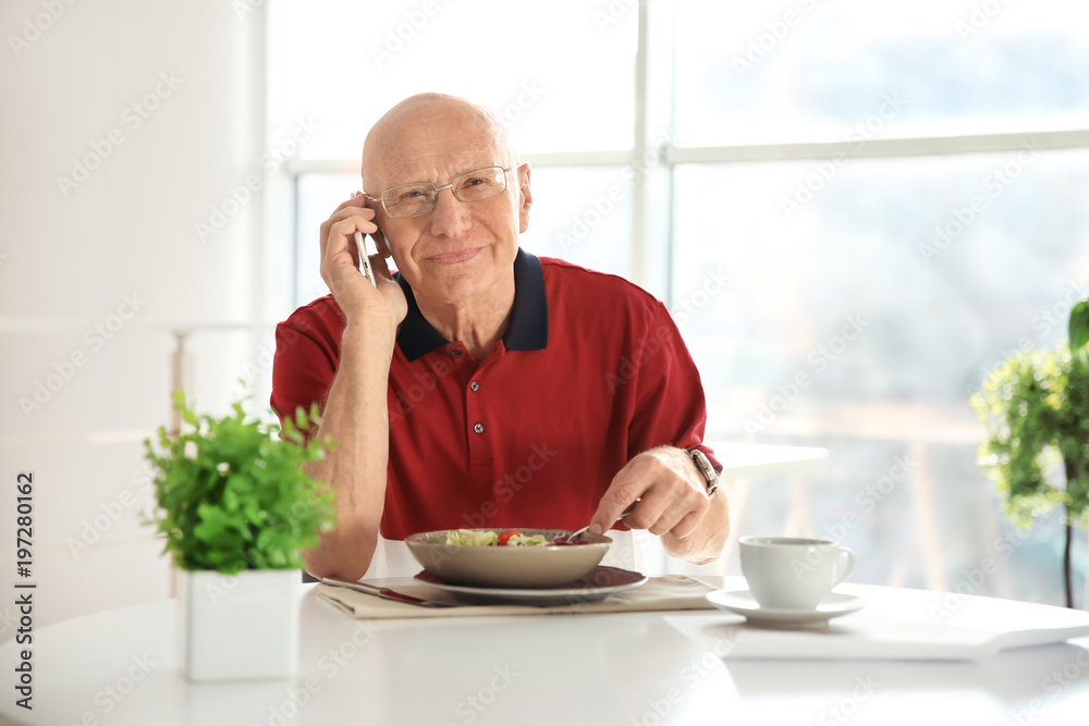 Elderly man talking on phone while having breakfast at home Elderly man talking on phone while having breakfast at home