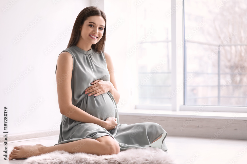 Young pregnant woman sitting on floor near window at home Young pregnant woman sitting on floor near window at home