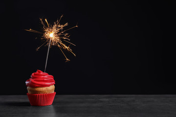 Delicious birthday cupcake with sparkler on table against black background