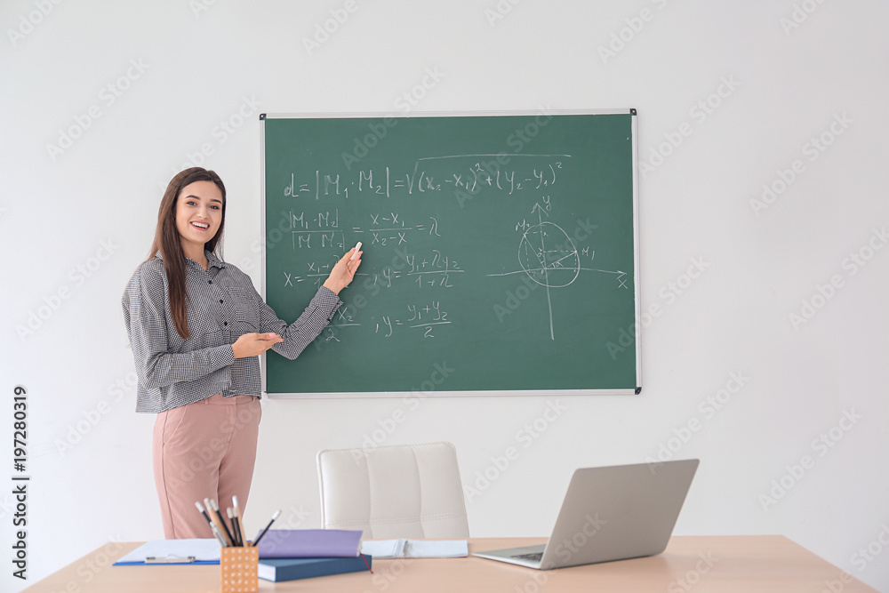 Young female teacher explaining material near blackboard in classroom Young female teacher explaining material near blackboard in classroom