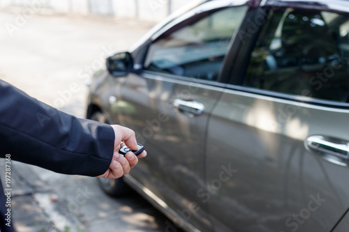 Business man holding car keys with car on background.