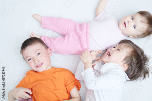 happy laughing kids, three children different ages lying, portrait of boy, little girl and baby girl, happiness in childhood of siblings, living in big family with three children