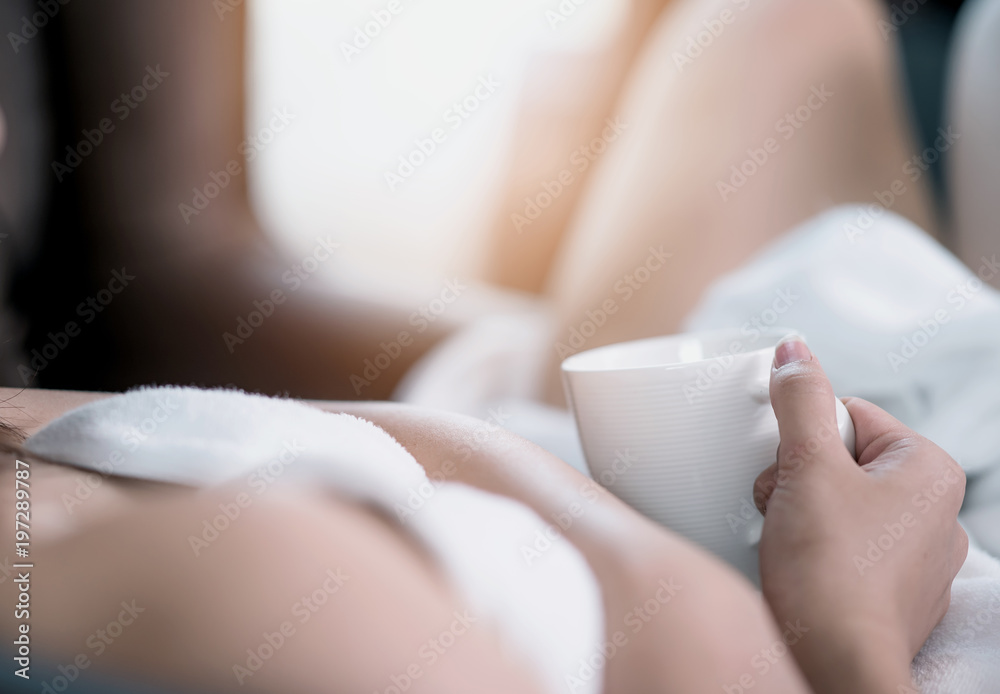 Close up woman in white towel holding coffee cup lying on the bed in morning time Close up woman in white towel holding coffee cup lying on the bed in morning time