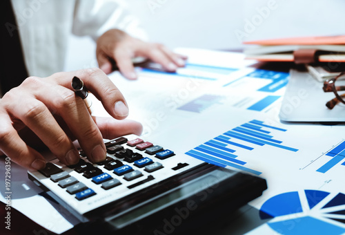 finance concept, business man holding pen using calculator with analyze graph chart and computer laptop for profit forecast in the future.